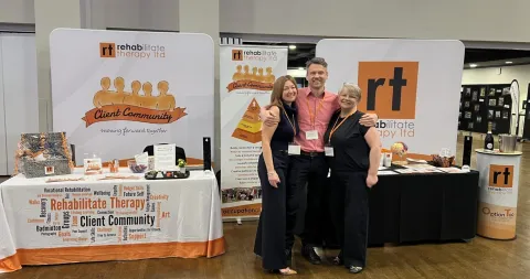 The Rehabilitate Therapy conference stand, with branded banners, a table cover and a pop-up stand, and three people in front.