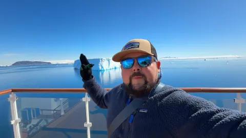 A selfie on a ship deck with a huge tabular iceberg behind.